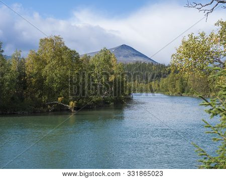 Beautiful Northern Landscape With Azure Blue River Kamajokk, Mountains, Boulders And Spruce Tree For