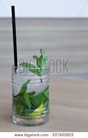Glass Of Mochito Cocktail On Wooden Table With Black Straw, Ice And Mint Leaf. Copy Space For Text. 