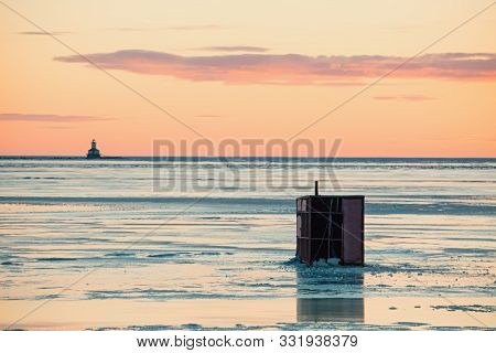 Ice fishing on a frozen harbor along the coast of rural Prince Edward Island, Canada. Lighthouse at the horizon.