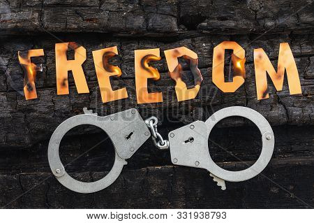 The Word Freedom Burns, And Handcuffs Lie Nearby. Burning Letters Made Of Paper. Concept On The Topi