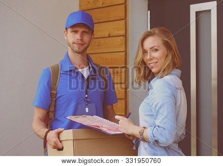 Smiling Delivery Man In Blue Uniform Delivering Parcel Box To Recipient - Courier Service Concept. S