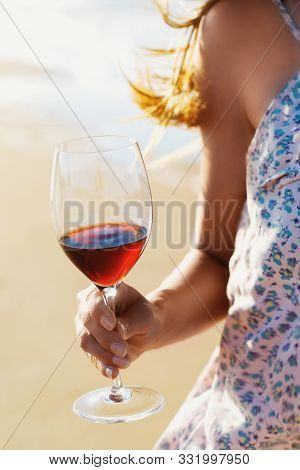 Glass Of Red Wine In The Hands Of A Girl Against The Backdrop Of A Coastline, Close-up