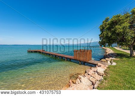 Beautiful Beach With A Small Empty Wooden Pier On Lake Garda (lago Di Garda) Between The Small Villa