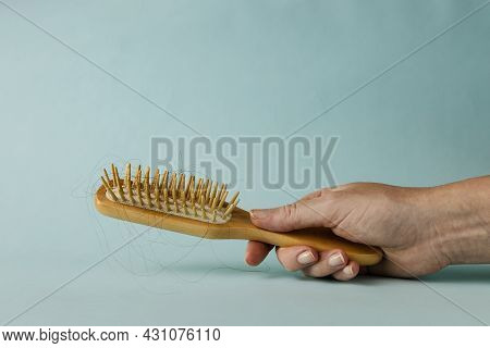 A Wooden Hairbrush With Hair In Womans Habd On Light Blue Backgraound With Copy Space