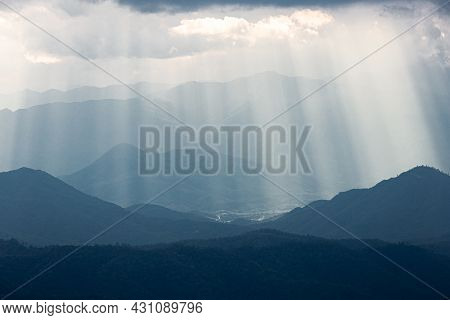 Dramatic Sunlight From Cloudy Sky Shining To Dark Blue Mountain Range.