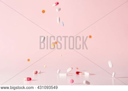 Various colorful pills dropped from top. Medicines jumped on table. Pink background. Selective focus