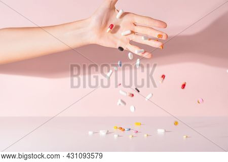 Various colorful pills dropped from top. Medicines jumped on table. Pink background. Selective focus