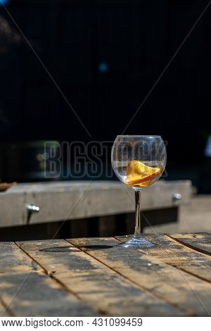 Vertical Photo Of Empty Wine Glass On Wooden Table. Unfilled Cut-glass With Orange Slice At Rustic W