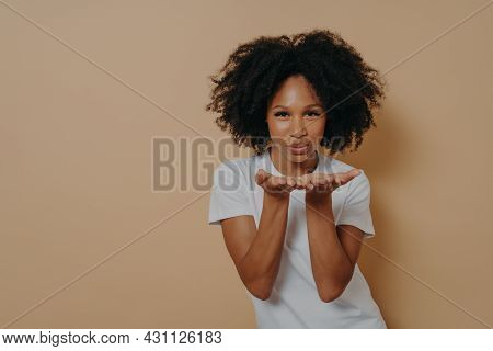 Beautiful Curly Flirty African Woman In White T-shirt Sending Air Kiss And Smiling, Demonstrating Wa