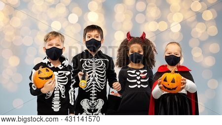 holiday, health and pandemic concept - children in halloween costumes and black reusable masks trick-or-treating over grey background