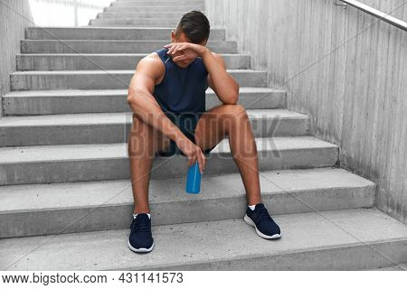 fitness, sport and people concept - tired young man with bottle of isotonic energy drink sitting on stairs