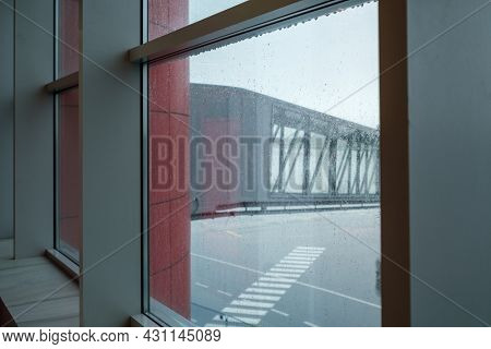 Modern jetway located on airfield behind wet window of aerodrome on rainy day