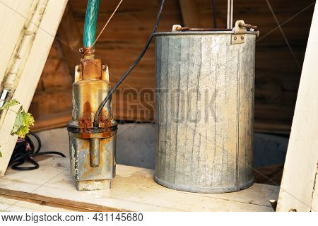 Electric Well Pump And A Metallic Bucket Stnding In The Country Well