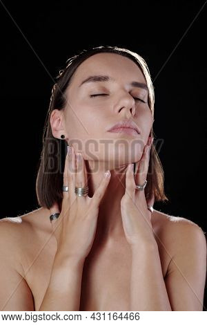 Sedactive young model with closed eyes demonstrating accessories on fingers against black background