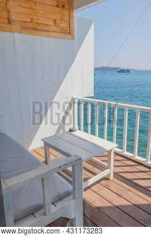 A View Of The Resort's Balcony Overlooking The Sea, Where The Terrace Features Wooden Sofas And Whit