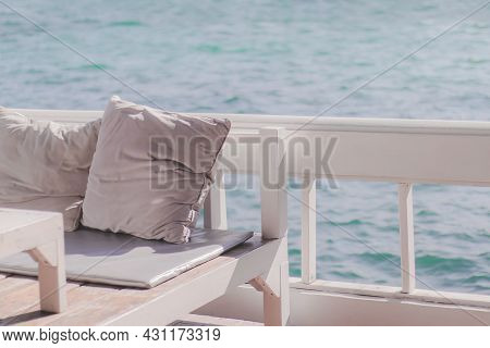 Two Pillows On The Wooden Sofa Of The Resort Terrace And Behind The Ocean Waves.