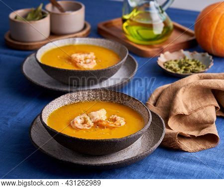 Pascetarian Pumpkin And Carrot Cream Puree Soup With Shrimps And Herbs In Bowl On Blue Linen Tablecl