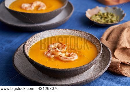 Pascetarian Autumn Pumpkin And Carrot Cream Puree Soup With Prawn And Condiment In Bowl On Blue Line