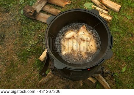 Frying Chicken In Black Cazan With Boiling Oil In Wood-burning Stove On Nature. Two Halves Of Chicke