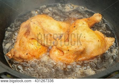 Frying Chicken In Black Cazan With Boiling Oil In Wood-burning Stove On Nature. Two Ruddy Tasty Halv