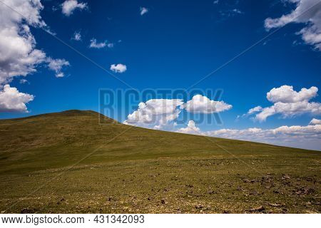 Green Mountain Hillside In Remote Area In The Rocky Mountains Against Blue Sky And White Clouds.