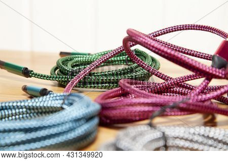 Pink Charging Cord In The Middle Of Green, Blue, And Silver Charging Cords On A Wooden Table