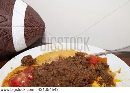 Spicy Ground Beef On A White Plae With Diced Tomatoes And Shredded Cheese Next To A Football