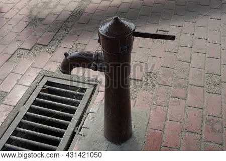 One Old Brown Iron Pump In The Pump Room For Pumping Water On The Sidewalk By The Metal Grate