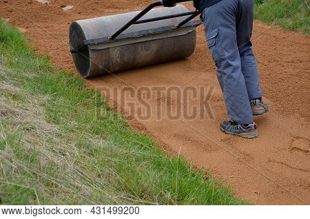Compressing The Gravel Of The New Park Threshing Path. Lawn Seed Is Repaired By Rolling A Metal Hand