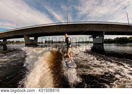 Armless Man Rides Wave On Wakeboarding Board Against The Background Of Bridge
