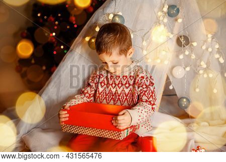 Little Kid Having Fun Near Decorated Tree Indoors. Surprised Cute Child Opening A Christmas Present.