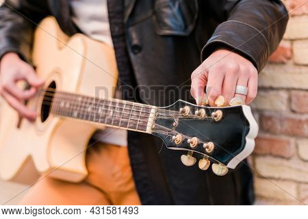 Street musician close up tuning the guitar. Fingers turning the tuning pegs of an acoustic guitar
