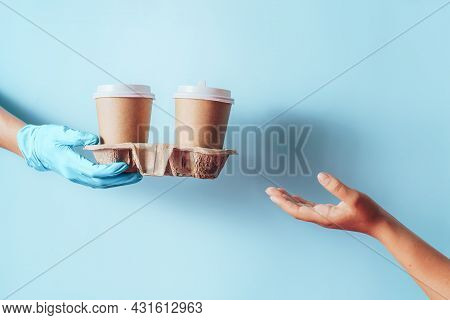 Hand In Blue Glove Passes Paper Coffee Cups To The Other Hand Against Blue Background.