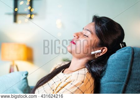 Young Girl With Closed Eyes Resting By Leaning On Sofa By Listening Favourite Song On Wireless Headp