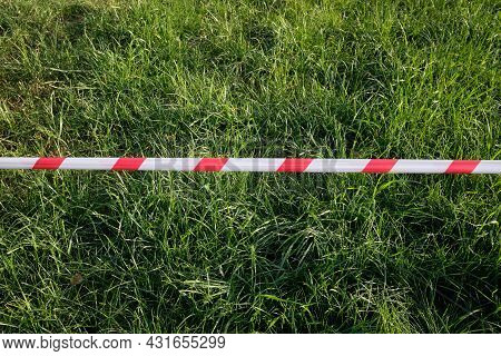 A Red And White Restraining Tape Over The Green Grass Of The Lawn. Restricting Access To The City Pa