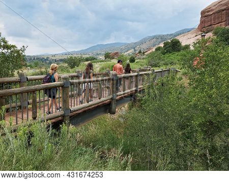Five Young Hikers Cross Bridge On Red Rocks Trading Post Trail Near Morrison, Colorado Under Dramati