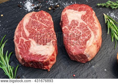 Raw Ribeye steaks with salt and herbs on grey board. Top view.