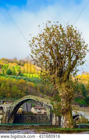 The old name of the bridge is Devil's Bridge. Italy, Lucca. The emerald cold water of the river reflects the ancient asymmetrical arches of the bridge. The Serchio River.