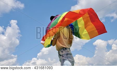 Blonde Woman Holding A Rainbow Lgbt Gender Identity Flag On Sky Background With Clouds Without Face 