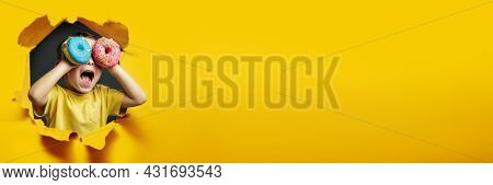 Happy cute boy is having fun played with donuts on Yellow background wall. Bright photo of a boy. Colored donuts