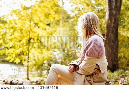 Lonely Upset Woman Wearing Cozy Warm Knitted Sweater And Coat Sit In Park At Autumn Sunny Day