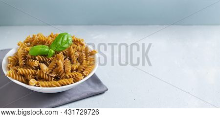 Raw Fusilli In A White Bowl On A Gray Napkin With A Sprig Of Basal On A Gray Background. Time To Eat