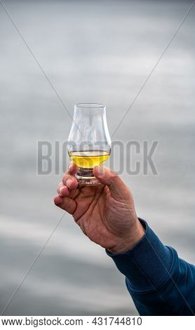 Hand With Dram Of Single Malt Scotch Whisky On Seashore In Scotland