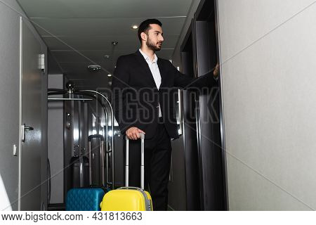 Bellboy In Suit Standing Near Luggage And Knocking Door In Hotel