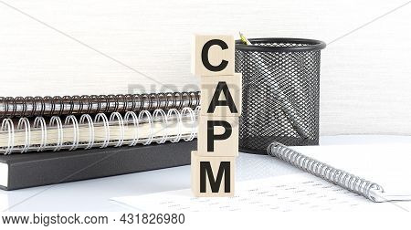 Capm Text On Wooden Block With Notebooks On The White Background