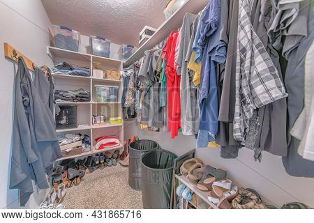 Small Messy Walk-in Closet With A Lot Of Shoes On The Carpet Floor