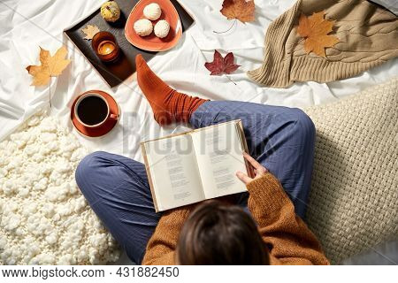 people, season and leisure concept - young woman reading book at home in autumn