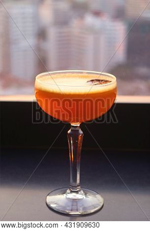 Closeup A Glass Of Vibrant Orange Cocktail At The Rooftop Terrace With Blurry Urban View In Backgrou