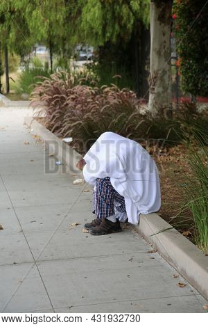 Los Angeles, California. August 17, 2021: Los Angles Homeless person talks to himself as he sits on a sidewalk covered with a sheet. The Homeless crisis is very terrible in Los Angeles California.
