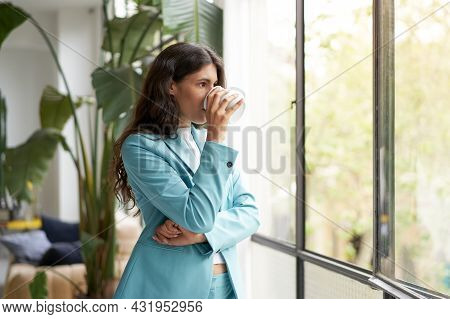 Young Businesswoman Enjoying Her Morning Coffee Or Tea, Looking Out The Window. Beautiful Latina Wom